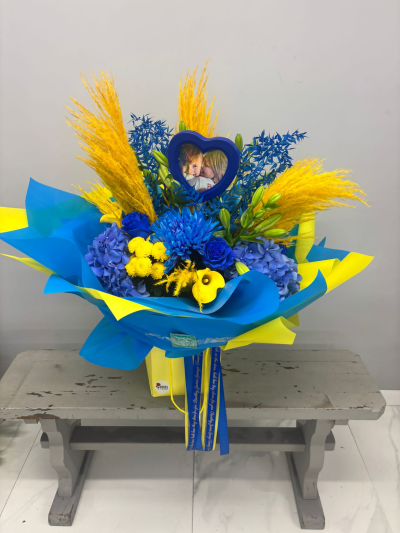 Golden Skies - Inspired by rich blue and golden tones, this eye-catching bouquet combines premium seasonal blooms with lush greenery and decorative textures. Beautifully gift-wrapped and presented in a matching box, it's designed to make a memorable statement for any special occasion.