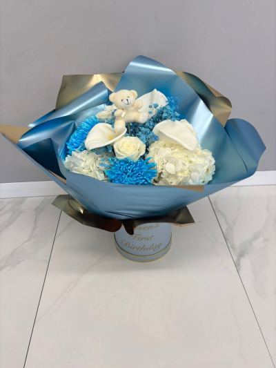 Baby Blue - A luxurious floral arrangement showcasing fresh seasonal blooms in calming blue and white hues, paired with an adorable plush teddy bear for a lasting keepsake. Beautifully wrapped in premium packaging, this elegant gift is designed to celebrate precious new beginnings and unforgettable moments.