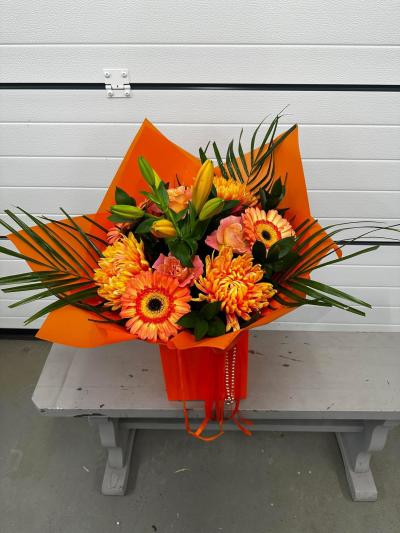 Citrus Sunrise - A bold and uplifting hand-tied bouquet presented in a vibrant orange gift box and wrapped in coordinating contemporary packaging with elegant ribbon detailing. Bursting with radiant shades of orange, golden yellow, soft peach, and fresh green foliage, this eye-catching arrangement captures the warmth and energy of a glowing sunrise. Its modern design and cheerful colour palette make it a perfect choice for birthdays, congratulations, thank-you gifts, celebrations, get-well wishes, or simply brightening someone's day with a vibrant display of joy.
