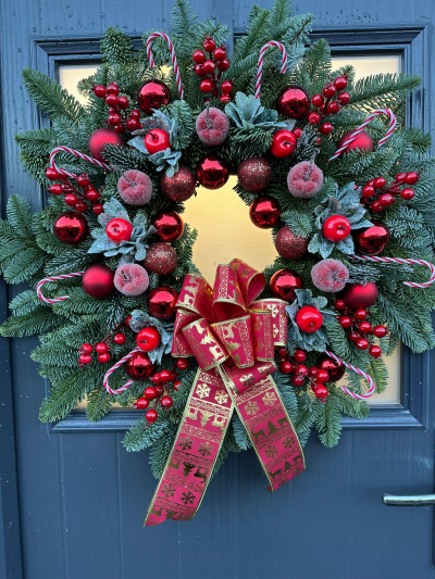 Candy Cane Christmas Wreath - Bring timeless festive cheer to your home with the Candy Cane Christmas Wreath. Handcrafted with fresh evergreen foliage, this eye-catching design is beautifully decorated with frosted seasonal accents, vibrant red berries, shimmering baubles, decorative candy canes, and a luxurious festive ribbon. Rich in traditional Christmas colours and classic holiday charm, this wreath is the perfect way to create a warm and welcoming entrance throughout the festive season.