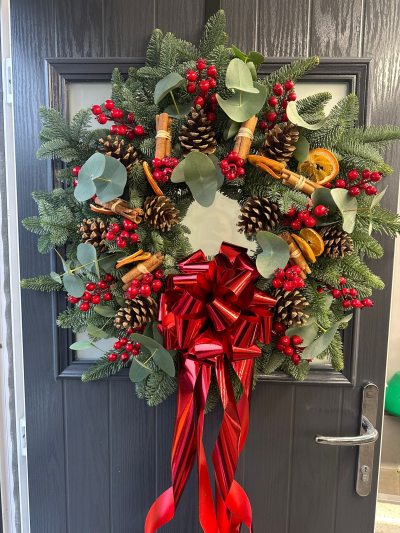 Rustic Christmas - Bring timeless festive charm to your home with the Rustic Christmas Heritage Wreath. Crafted with fresh evergreen foliage, this traditional design is beautifully accented with natural pine cones, aromatic cinnamon bundles, dried citrus slices, vibrant red berries, soft eucalyptus foliage, and finished with a luxurious metallic red bow. Blending rustic textures with classic Christmas colours, this handcrafted wreath creates a warm and welcoming display for your front door throughout the festive season.