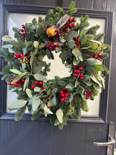 Woodland Robin - Celebrate the beauty of a traditional winter woodland with the Woodland Robin Christmas Wreath. Handcrafted with fresh evergreen foliage, this elegant design is adorned with vibrant red berries, soft eucalyptus, natural pine accents, and a charming robin perched at the top for a delightful seasonal touch. Its natural textures and classic festive colours create a warm, welcoming display that brings timeless Christmas charm to any front door.