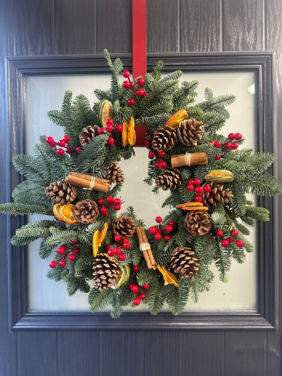 Rustic Citrus & Cinnamon - Welcome the festive season with the warm charm of the Rustic Citrus & Cinnamon Christmas Wreath. Handcrafted with fresh evergreen foliage, this natural design is beautifully decorated with aromatic cinnamon bundles, dried orange and lime slices, natural pinecones, and vibrant red berry accents. Inspired by the cosy scents and textures of Christmas, this elegant wreath brings a traditional woodland feel to your front door and creates a warm, inviting welcome throughout the holiday season.