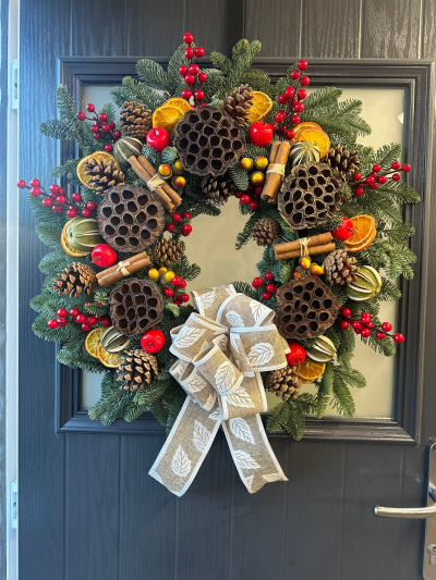 Rustic Harvest - Bring the warmth of a traditional countryside Christmas to your home with the Rustic Harvest Christmas Wreath. Handcrafted with fresh evergreen foliage, this beautifully textured design features natural pinecones, dried orange slices, cinnamon bundles, seed pods, decorative fruits, vibrant red berry accents, and a rustic linen-style bow. Combining earthy tones with festive colour, this elegant wreath creates a cosy and welcoming display that perfectly captures the charm of the Christmas season.